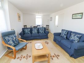 A living room with two blue sofas and one blue armchair with patterned cushions a wooden coffee table and a dining table with chairs at La Capsule in Dawlish Warren