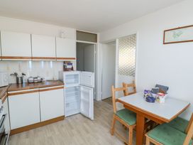 A kitchen with white cabinets an open refrigerator and a dining table with green cushioned chairs at La Capsule in Dawlish Warren