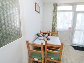 A dining area with a table and four wooden chairs near a window and door at La Capsule in Dawlish Warren