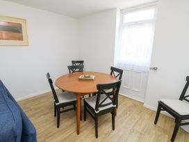 A dining area with a round wooden table and four black chairs with white cushions next to a white door with a curtain at La Capsule in Dawlish Warren