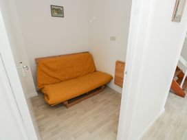 A small room with a mustard yellow futon and a small foldable wooden table on the wall at La Capsule in Dawlish Warren