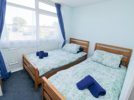 A bedroom with two single wooden beds covered with patterned bedding and blue towels near a window with blue curtains at La Capsule in Dawlish Warren