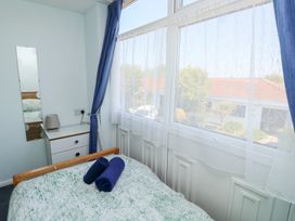 A bedroom with a bed covered in patterned bedding with two rolled towels a bedside table with a lamp a tall mirror on the wall and windows with sheer curtains and blue drapes at La Capsule in Dawlish Warren
