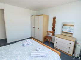 A bedroom with a bed covered with a patterned blanket and towels a wardrobe a dresser with a mirror a wooden chair and a heater at La Capsule in Dawlish Warren