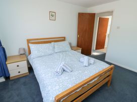 A bedroom with a wooden double bed with blue floral bedding and striped towels two wooden bedside tables with lamps and a wooden door at La Capsule in Dawlish Warren