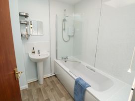 A bathroom with a bathtub a sink a mirror and a wall-mounted shelf at La Capsule Dawlish Warren