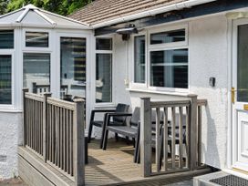 A deck area with chairs next to windows and a door at Mylnebeck Lodge in Bowness-on-Windermere