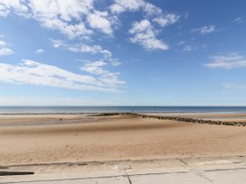 A sandy beach with a rock jetty extending into the sea under a blue sky at Fairways in Prestatyn
