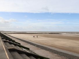 A beach with three people walking on the sand near a concrete promenade and sea defenses at Fairways in Prestatyn