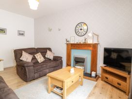 A living room with brown sofas a wooden coffee table a fireplace with decorations a wall clock and a television on a stand at Fairways in Prestatyn