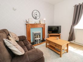 A living room with a brown sofa a wooden coffee table a wooden fireplace with a clock and decor and a television on a stand at Fairways in Prestatyn