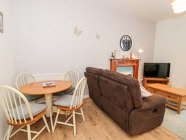A living room with a brown sofa a round wooden dining table with four chairs a wooden coffee table a television and a decorative fireplace at Fairways in Prestatyn