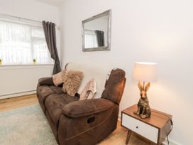 A brown sofa with cushions and a white throw next to a wooden side table with a lamp featuring a rabbit base at Fairways in Prestatyn