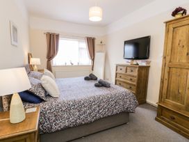 A bedroom with a double bed floral bedspread bedside tables lamps wooden dresser wardrobe and a wall mounted TV at Fairways in Prestatyn