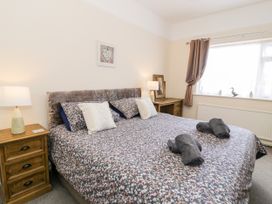 A bedroom with a large bed with floral bedding two bedside tables with lamps a window with curtains and a framed picture on the wall at Fairways in Prestatyn