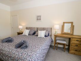A bedroom with a double bed with floral bedding two bedside tables with lamps and a wooden dressing table with a stool