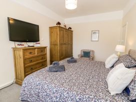 A bedroom with a bed covered in floral bedding two rolled towels on the bed a wooden chest of drawers with books on it a wall-mounted TV a wooden wardrobe and a plaid armchair with a cushion at Fairways in Prestatyn