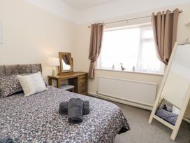 A bedroom with a bed covered in floral bedding next to a wooden dressing table and a window with curtains at Fairways in Prestatyn