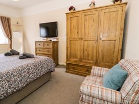 A bedroom with a bed covered with floral bedding three rolled towels a wooden chest of drawers with books and a wall-mounted TV a large wooden wardrobe a plaid armchair with a blue cushion and a wall mirror at Fairways in Prestatyn