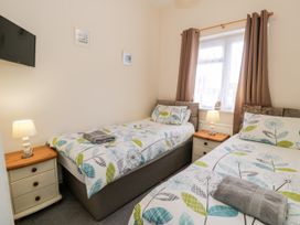 A bedroom with two single beds bedside tables and a wall-mounted TV at Fairways in Prestatyn