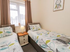 A bedroom with two single beds a nightstand with a lamp between them and a window with curtains at Fairways in Prestatyn