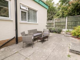 An outdoor patio area with wicker chairs and a glass table next to a house with a window and garden fence at Fairways in Prestatyn