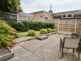 A fenced backyard with a paved patio area, outdoor chairs, a raised flower bed, and bushes at Fairways in Prestatyn