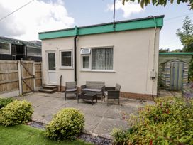 A small patio area with garden furniture and bushes in front of a single-story building with windows and a door at Fairways in Prestatyn