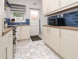 A kitchen with white cabinets blue tiled walls patterned floor and a microwave at Fairways in Prestatyn