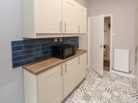 A kitchen with white cabinets wooden countertop blue tile backsplash black microwave patterned floor tiles and an open white door at Fairways in Prestatyn