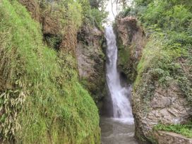 A waterfall flowing between rocky cliffs with green vegetation at Riverlea in Dyserth