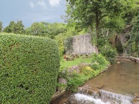 A garden area with picnic tables near a stone wall and a small river with a waterfall at Riverlea in Dyserth
