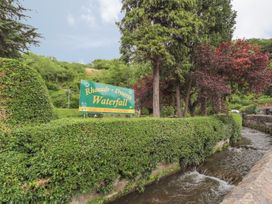 A green sign reading Rhaeadr Dyserth Waterfall next to a river and surrounded by trimmed hedges and trees at Riverlea in Dyserth