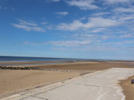 A beach with a concrete walkway and a railing with a few people walking on rocks near the shore at Riverlea in Dyserth
