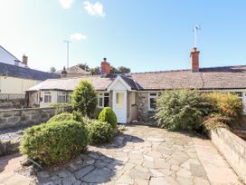 Front view of a single-story house with stone walls a white door and shrubs in the paved garden at Riverlea in Dyserth
