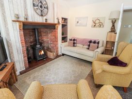 A living room with a lit wood stove fireplace two yellow chairs a cream sofa and wall clock at Riverlea in Dyserth
