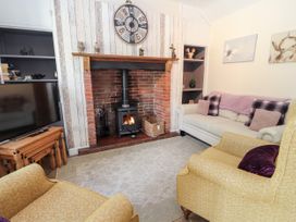 A living room with two yellow armchairs a white sofa a fireplace with a wood burning stove and a wall clock at Riverlea in Dyserth