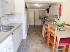 A kitchen with light wooden cabinets a dining table with wooden chairs and red cushions and a washing machine at Riverlea in Dyserth
