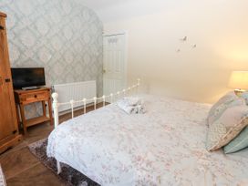 A bedroom with a bed with floral bedding a wooden wardrobe a wooden side table with a TV and a lamp on the right at Riverlea in Dyserth