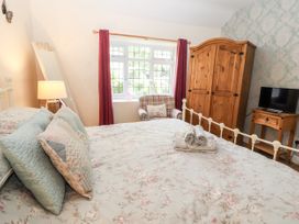 A bedroom with a bed with floral bedding pillows and towels a wardrobe a chair a table with a TV a standing mirror and a window with red curtains at Riverlea in Dyserth