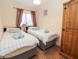 A bedroom with two single beds bedside table lamp wooden wardrobe and window with curtains at Riverlea in Dyserth