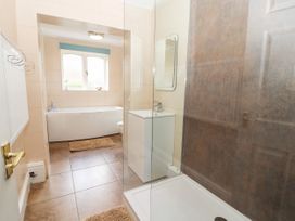 A bathroom with a bathtub under a window a shower area a white sink a mirror and brown tiled flooring at Riverlea in Dyserth