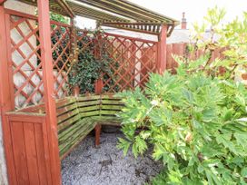 An outdoor wooden seating area with a lattice back surrounded by plants at Riverlea in Dyserth