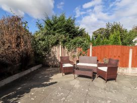 An outdoor patio with wicker chairs and a coffee table surrounded by wooden fences and plants at Riverlea in Dyserth