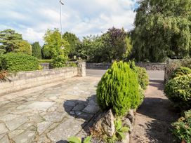 A paved driveway with bushes and trees along the sides leading to a road bordered by a stone wall at Riverlea in Dyserth
