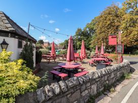 An outdoor seating area with red picnic tables and umbrellas beside a stone wall and a white building at Riverlea in Dyserth