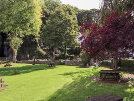 A grassy park area with picnic tables and trees including one with red leaves at Riverlea in Dyserth