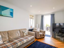 A living room with beige sofas a television and an open door leading to an outdoor seating area at Pink House in Mevagissey
