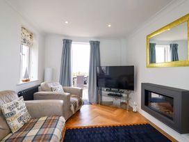 A living room with two armchairs a television on a glass stand a wall-mounted fireplace and a large mirror at Pink House in Mevagissey
