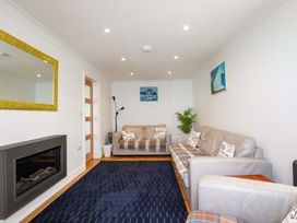 A living room with sofas, a blue rug, a wall-mounted fireplace, a yellow-framed mirror, and paintings at Pink House in Mevagissey
